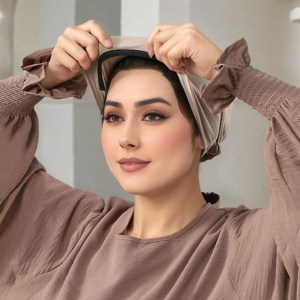 A woman wearing a beige inner hijab cap, adjusting it on her head.