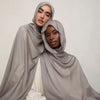 Une femme portant un foulard modal gris sourd et fluide avec un haut de couleur claire.