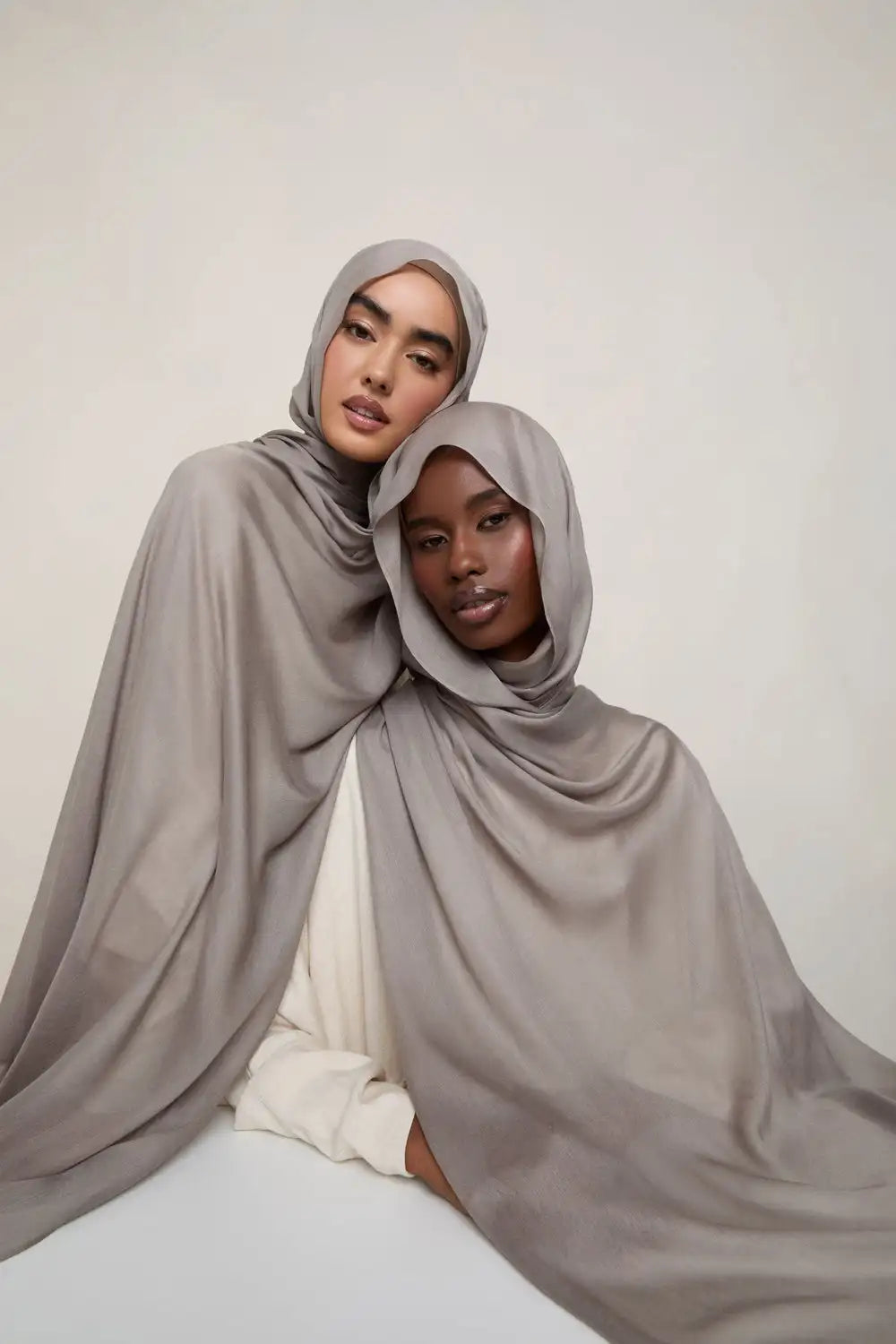 Une femme portant un foulard modal gris sourd et fluide avec un haut de couleur claire.