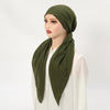 Une femme modèle un bonnet de hijab en lin vert olive drapé autour de son cou, associé à un haut blanc.