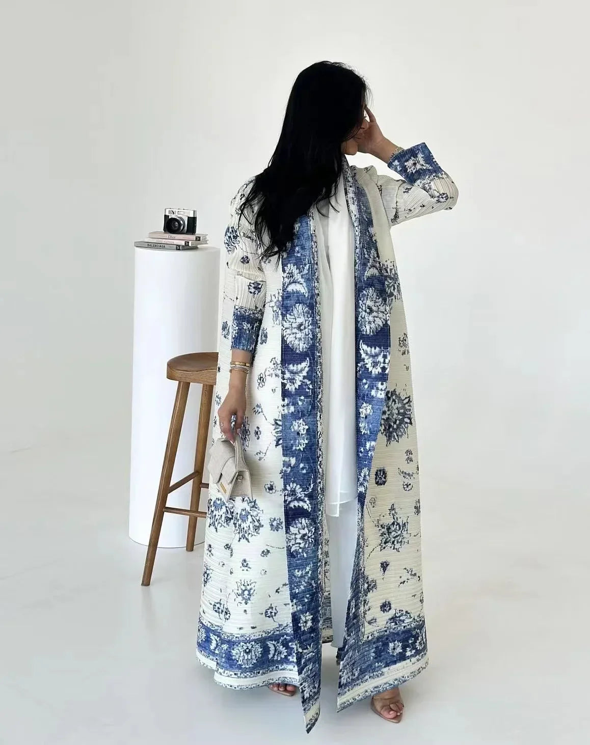 Une femme portant un trench-coat à manches longues plissé à motifs bleu et blanc dans un studio lumineux.