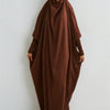 Eine Frau trägt eine braune, modische Abaya mit gerafften Ärmeln vor einer weißen Wand.
