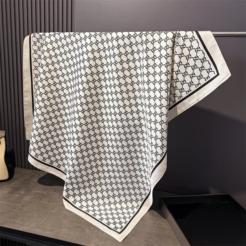 Weißer Seiderschal mit schwarzem geometrischem Muster auf dunklem Untergrund.