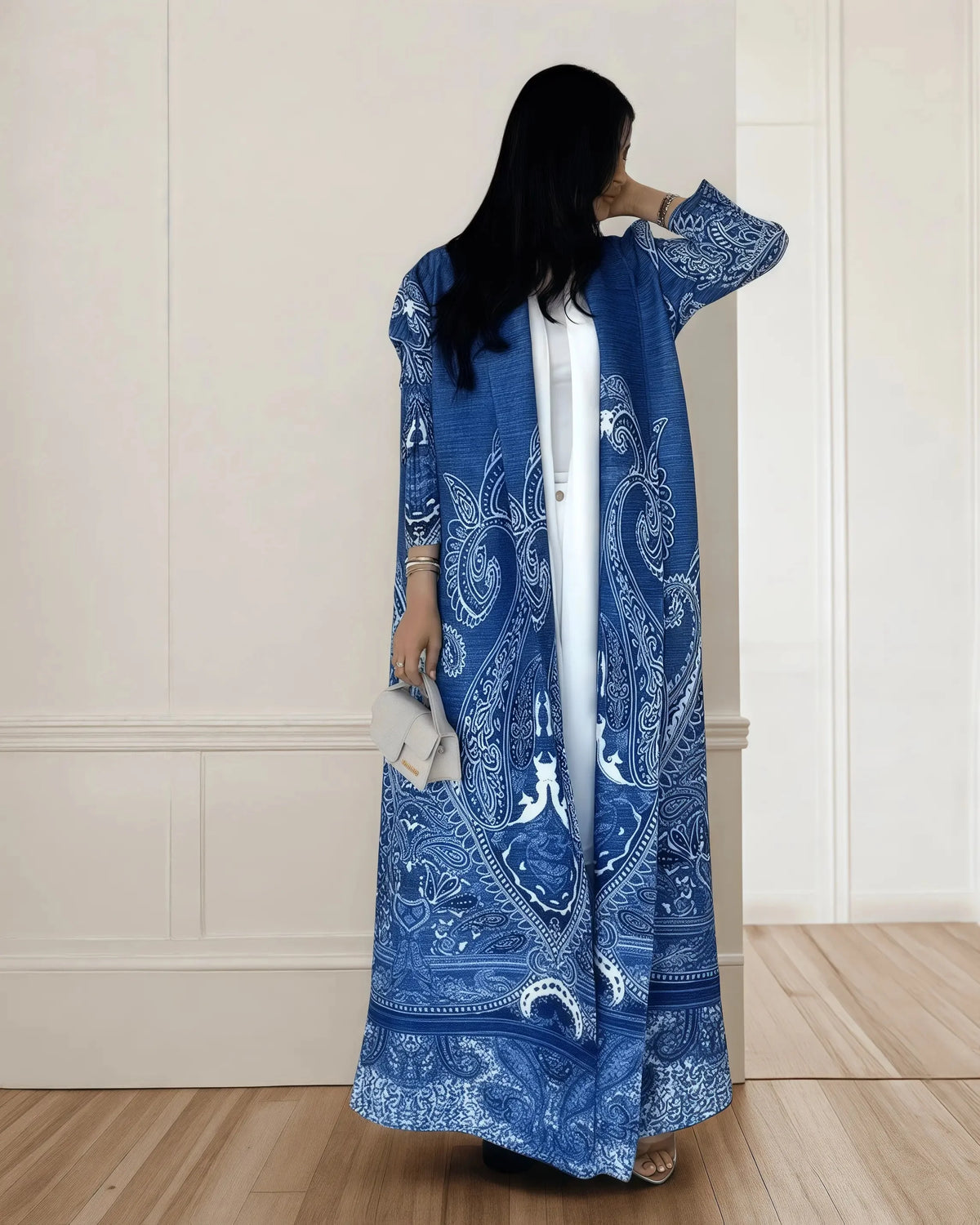 Una mujer vistiendo un cárdigan abaya plisado azul largo de hombreras, de pie en una habitación de color claro.