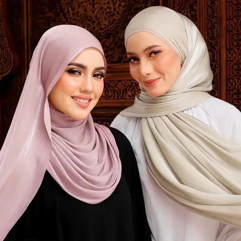 Dos mujeres vistiendo pañuelos de chifón arrugado brillantes en tonos rosa suave y beige.