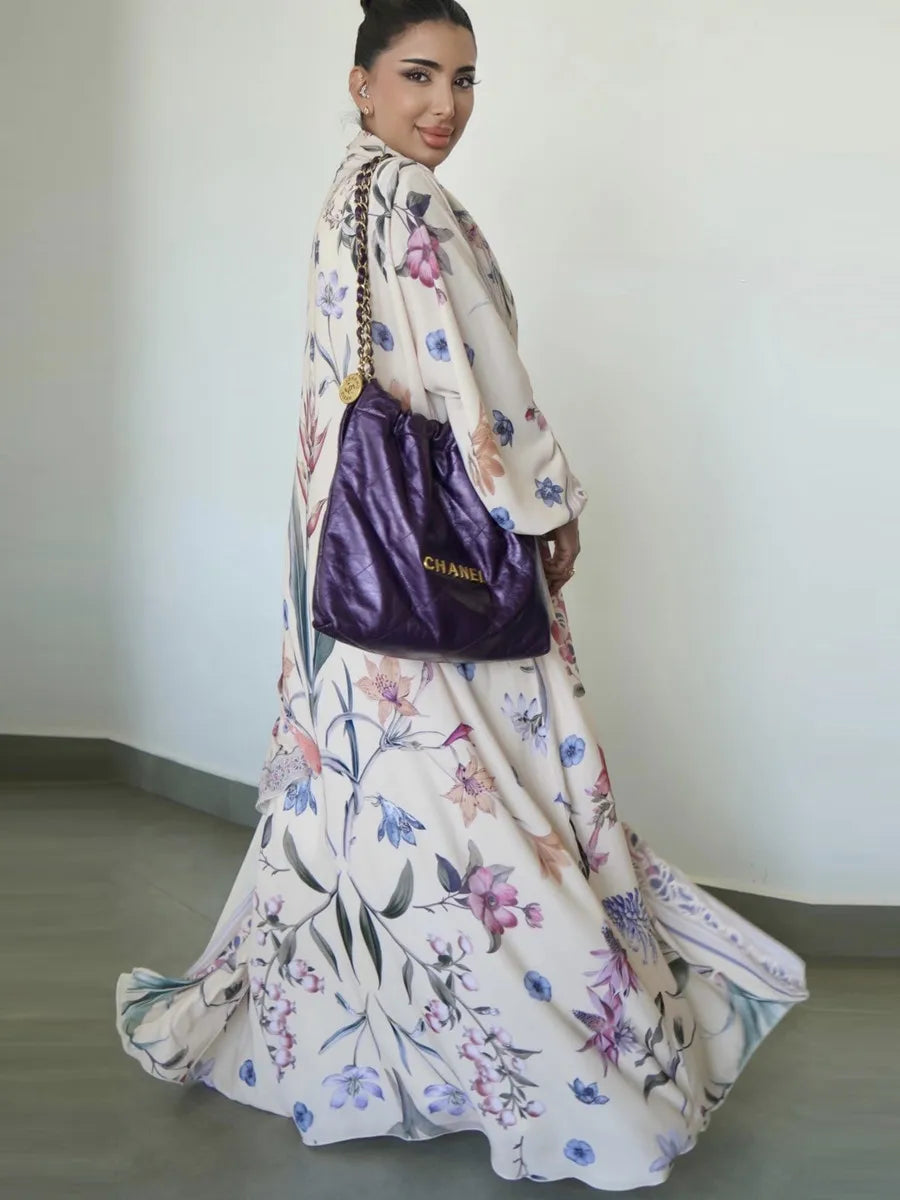 Una mujer vistiendo un caftán blanco largo y fluido con estampado floral, llevando un bolso morado.