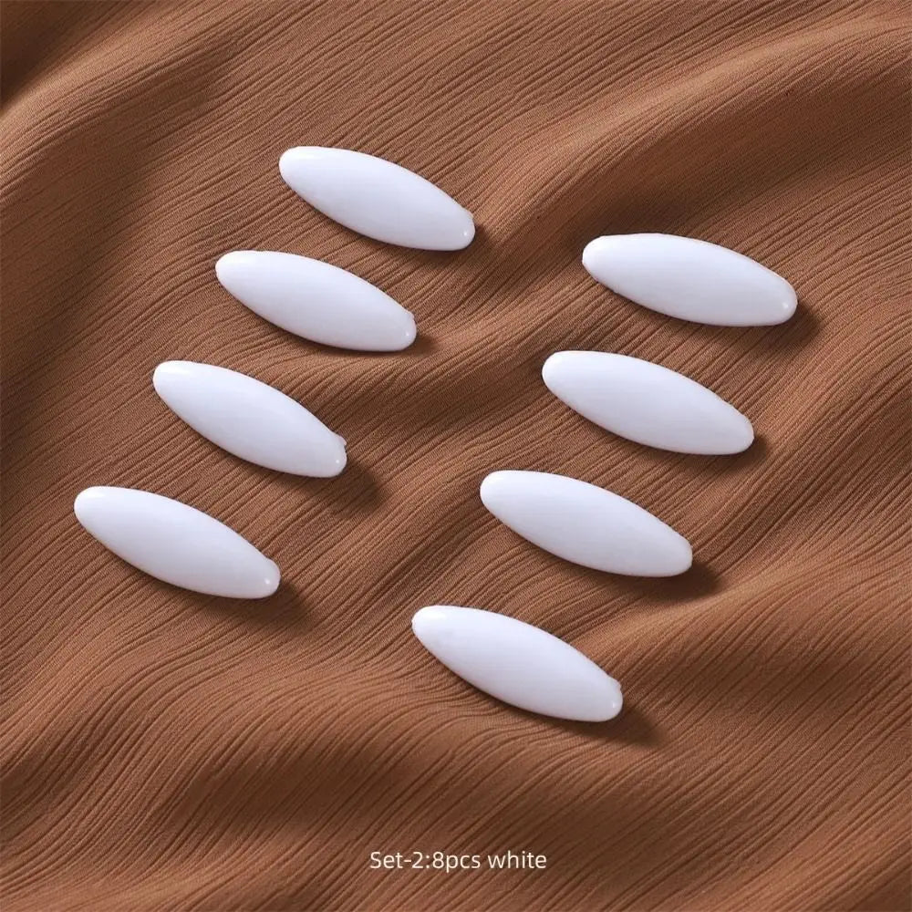 Eight white oval brooch pins arranged on a brown fabric background