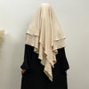 A woman wearing a beige two-layer everyday hijab scarf over a black top.