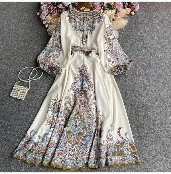 A white maxi dress featuring floral lace and embroidery with blue, pink, and gold accents.