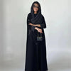 Eine Frau trägt ein schwarzes Abaya mit Polka-Dot-Muster und einem langen schwarzen Strickkleid.