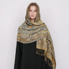 Una mujer vistiendo un pañuelo pashmina de lujo con patrón beige y dorado sobre una blusa negra.