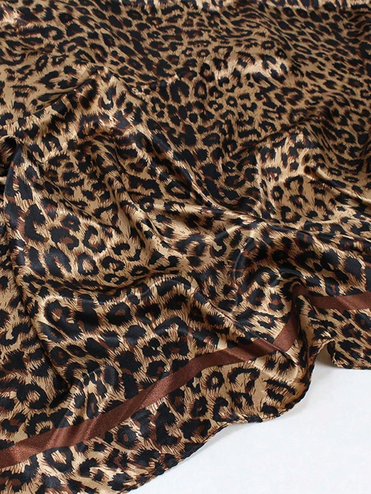 A close-up of a brown leopard print silk satin neckerchief hijab scarf fabric.