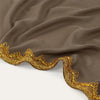 Nahaufnahme eines taupefarbenen Chiffonstoffs mit einem verzierten Goldverzierkantenrand.