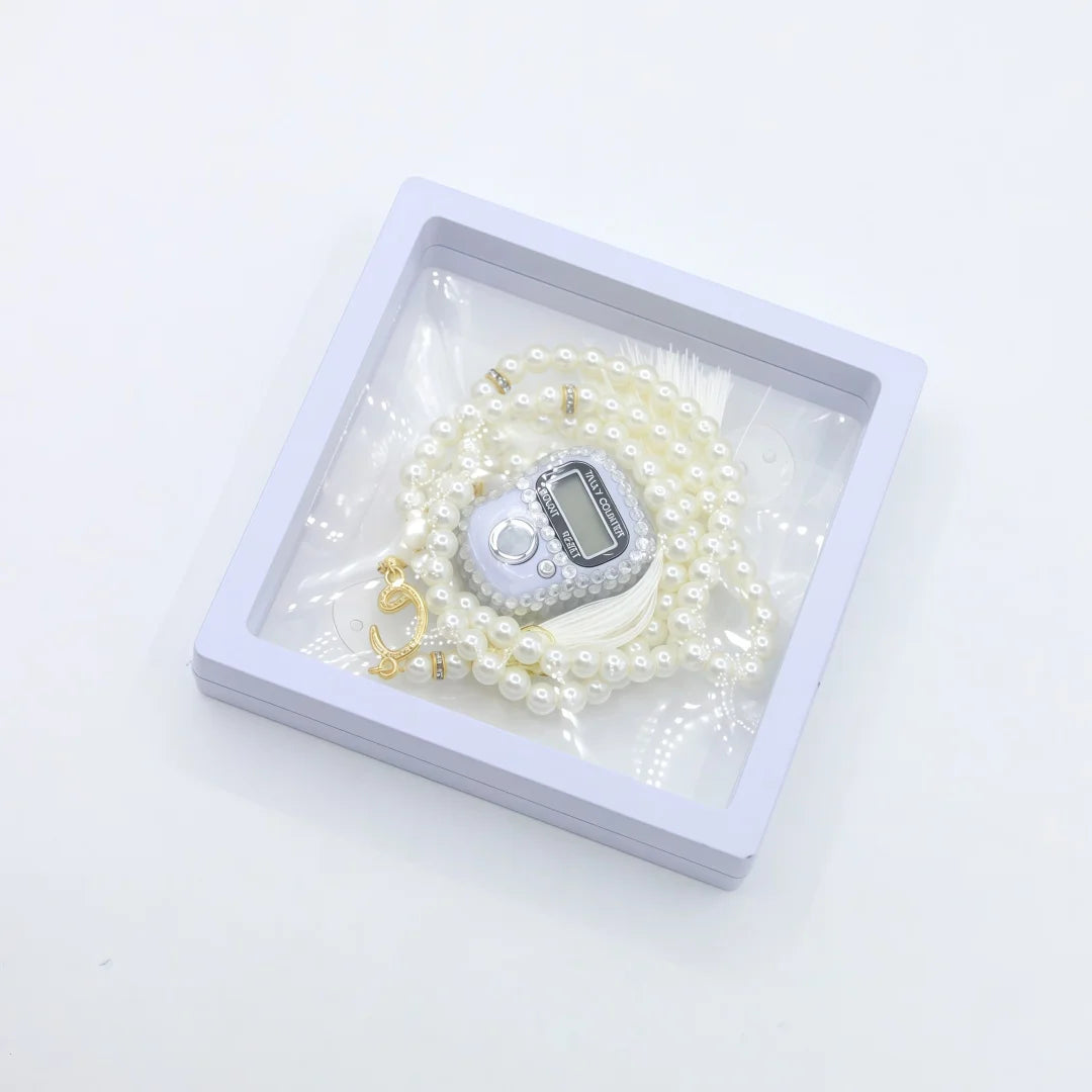 A silver digital counter bracelet is displayed in a white box surrounded by white prayer beads.
