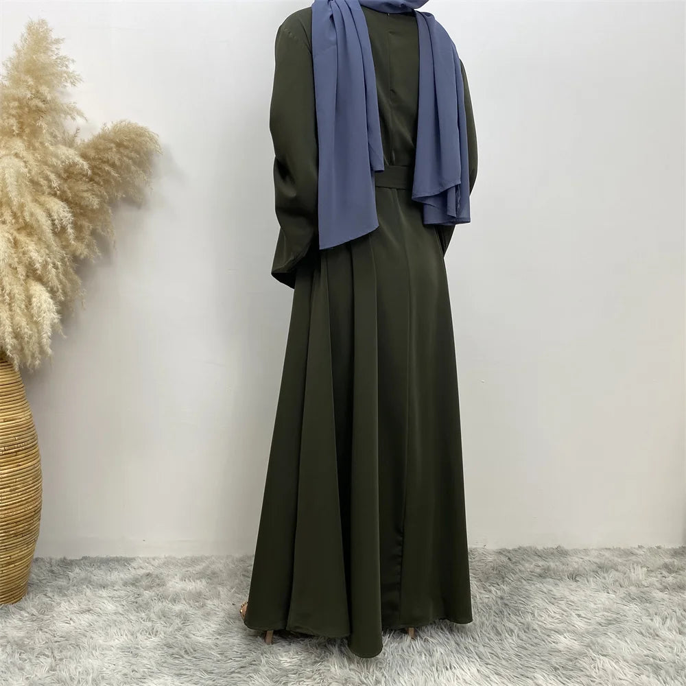 Vestido abaya verde oliva de largo completo con pañuelo morado a juego, exhibido contra una pared blanca.
