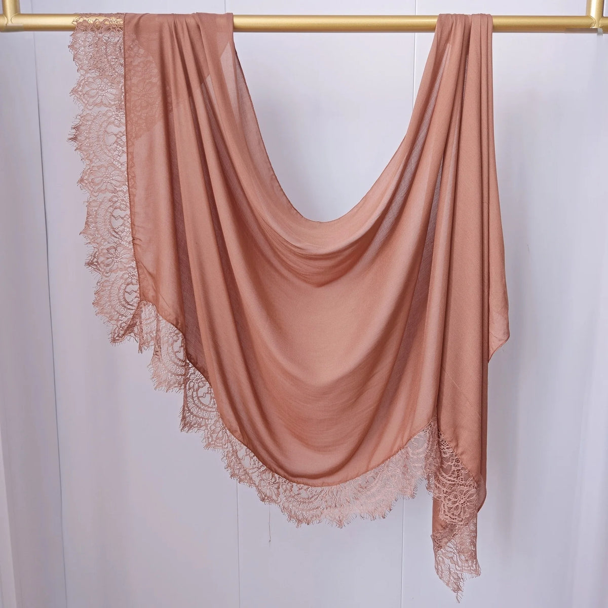 Hijab de encaje color rosa empolvado cayendo sobre un percha dorada.