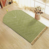 Alfombra de oración rectangular verde oliva con patrón geométrico grabado y borlas doradas sobre un suelo de madera clara.