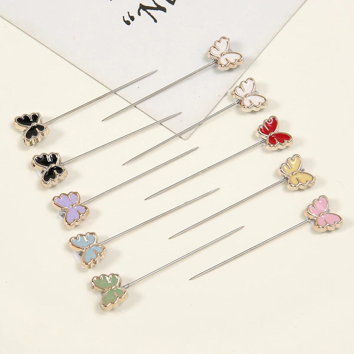 Un juego de delicados pines para hijab de plata con pequeños patrones de mariposas en varios colores.