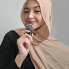 A woman wearing a beige hijab is holding a small microphone with a fuzzy windscreen.