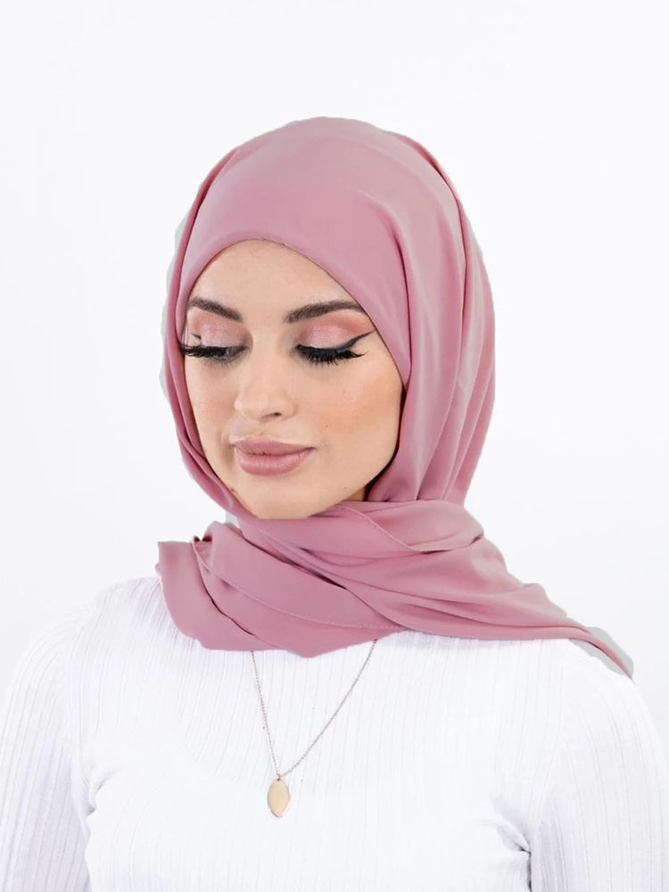 Une femme portant un hijab en mousseline rose poudré et un haut blanc.