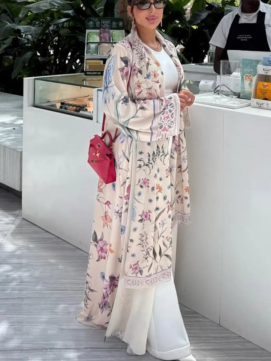 Una mujer vistiendo un caftán largo de estampado floral en tonos beige y rosa, de pie cerca de una mesa de exhibición.