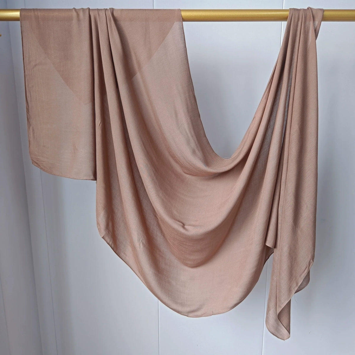 Foulard modal de couleur beige drapé sur un cintre en bois.