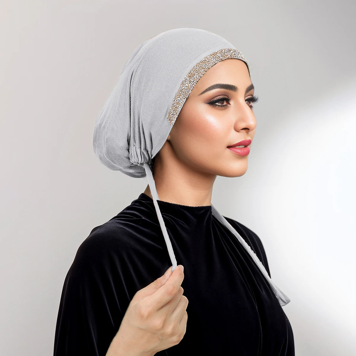 Eine Frau mit einem hellgrauen Strass-Hijab und einem schwarzen Samt-Oberteil, im Profil dargestellt.