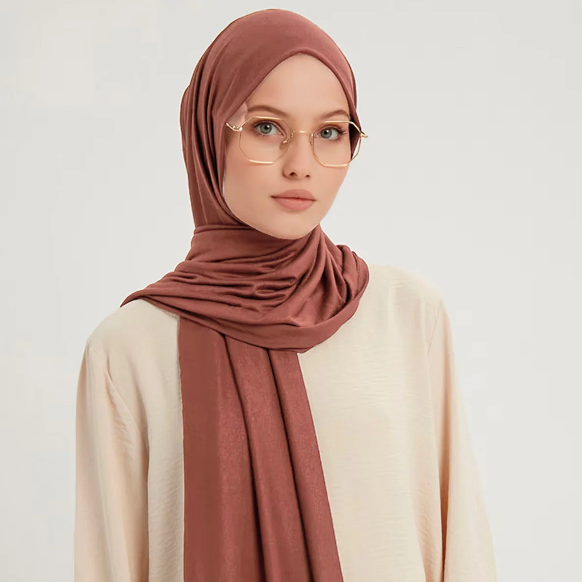 Una mujer vistiendo un pañuelo hijab de algodón premium elástico color rosa empolvado y una blusa beige clara.