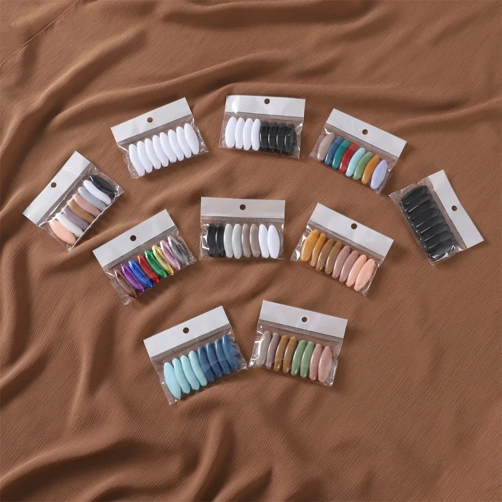 Eight sets of solid color brooch pins for scarves and hijabs arranged on a brown fabric.
