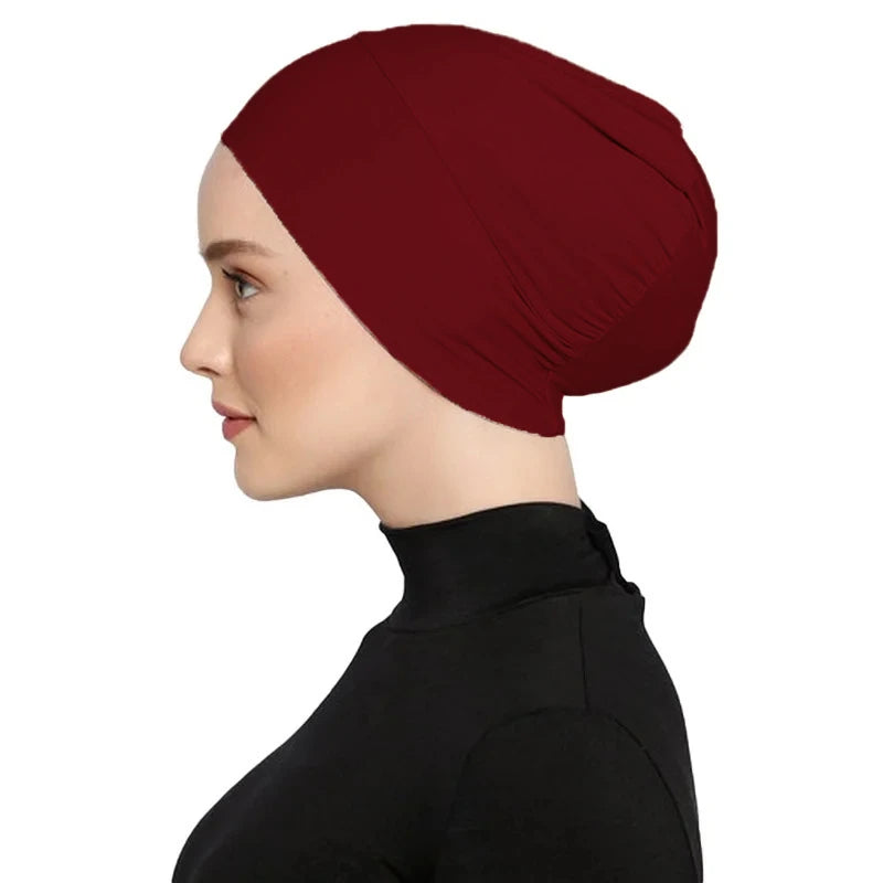Una mujer vistiendo un turbante instantáneo color granate oscuro con hijab y una blusa negra.