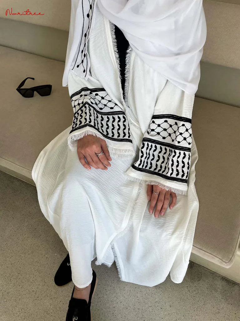 Une femme portant une abaya musulmane blanche brodée avec des bordures noires et des chaussures noires.