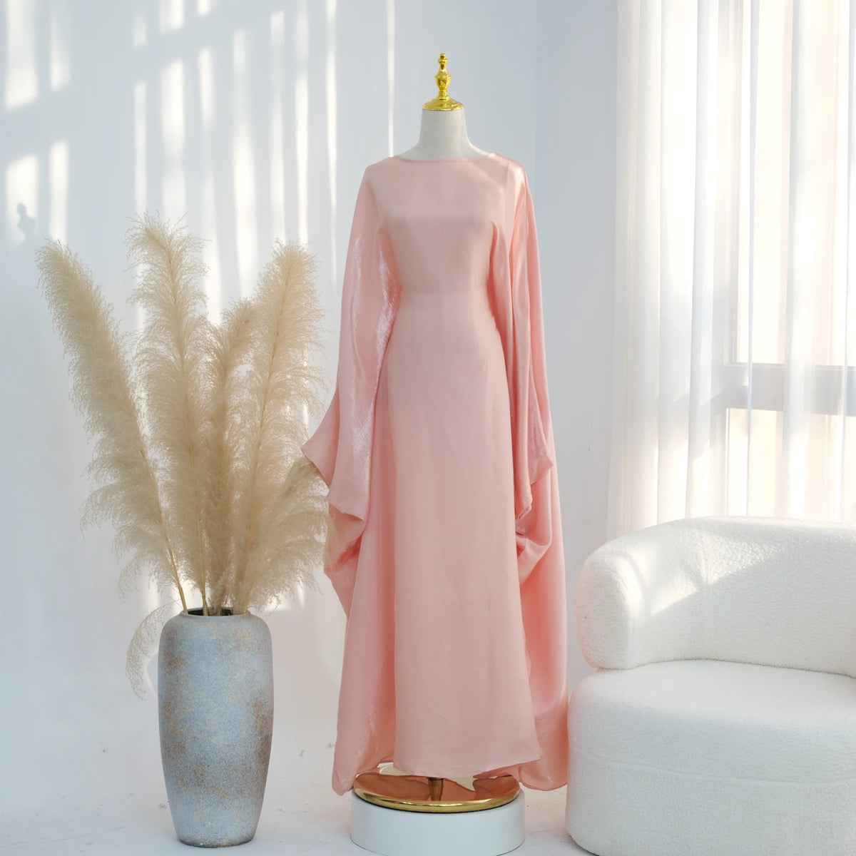 Ein pinkes, elegantes Kaftan-Kleid auf einem Mannequin neben getrocknetem Ziergräsern.