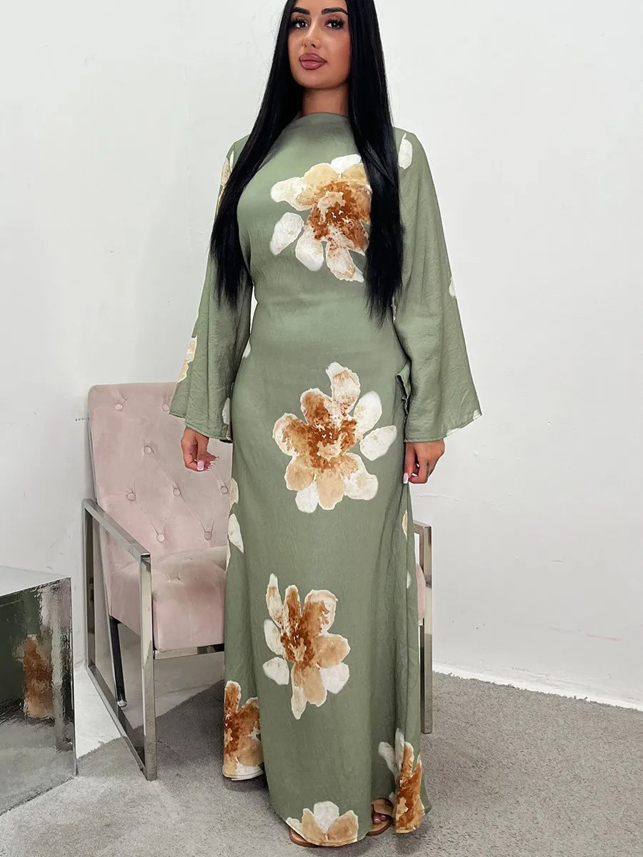 A woman models a long, olive green kaftan dress with a floral print and gold trim.