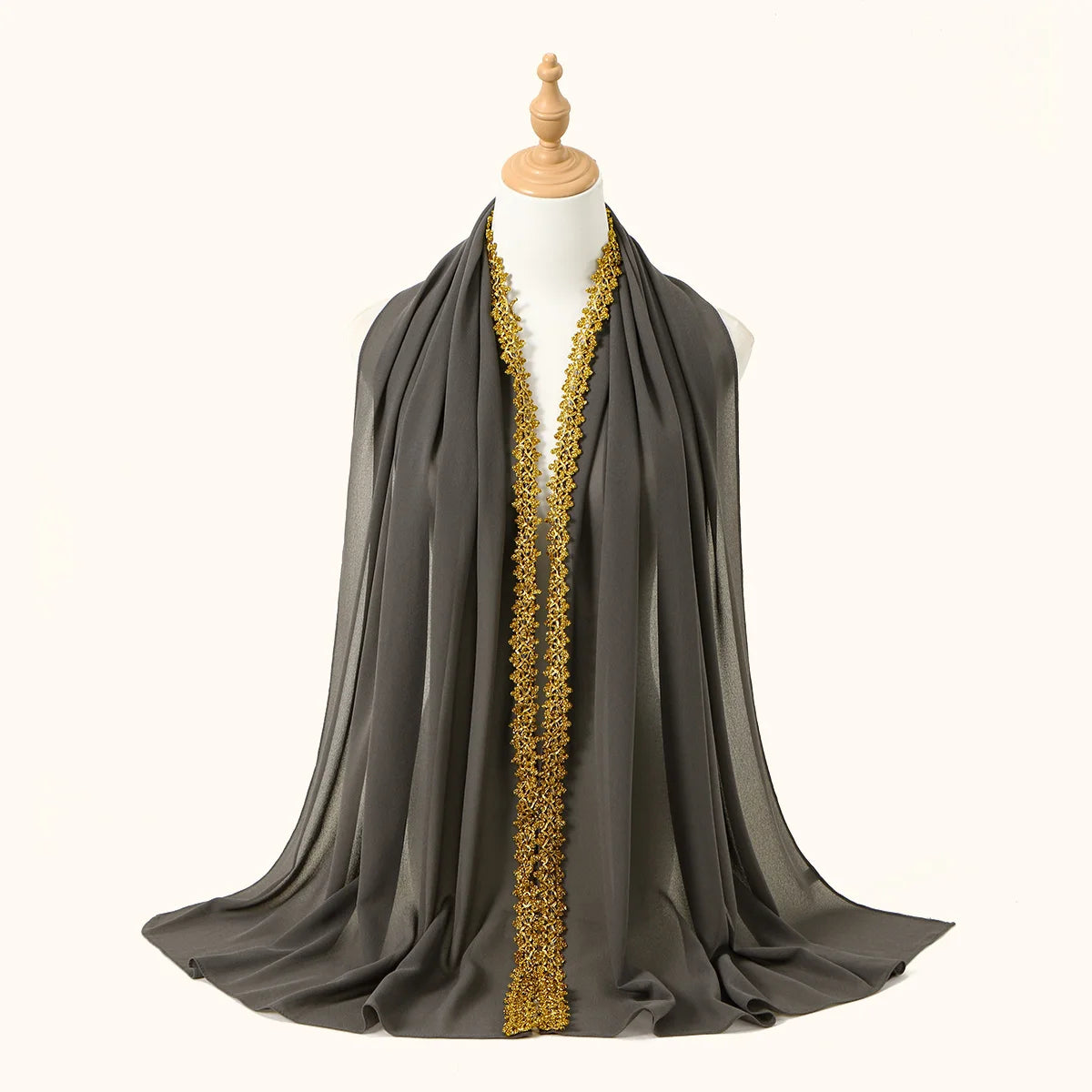 Pañuelo/chal de gasa gris oscuro drapeado sobre el cuello de un maniquí con ribete de strass dorados.