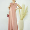 A woman models a flowing, pale pink modest abaya dress against a white background.