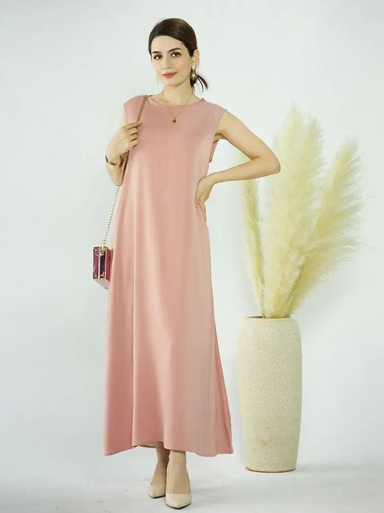 A woman models a flowing, pale pink modest abaya dress against a white background.