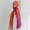Una mujer vistiendo un pañuelo de hijab fluido impreso con acuarela en tonos naranja y púrpura.