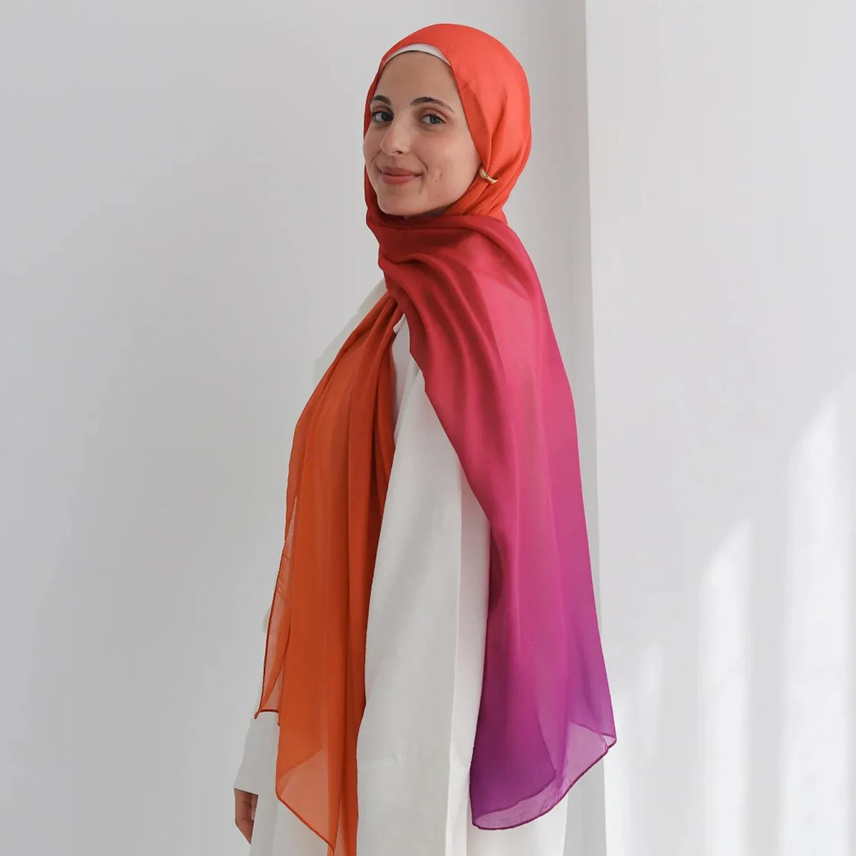 Una mujer vistiendo un pañuelo de hijab fluido impreso con acuarela en tonos naranja y púrpura.