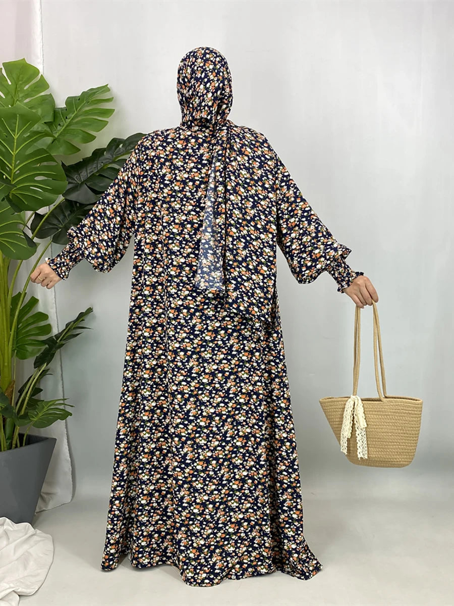 Una mujer vistiendo una elegante kaftan floral con hiyab, de pie en un estudio luminoso.