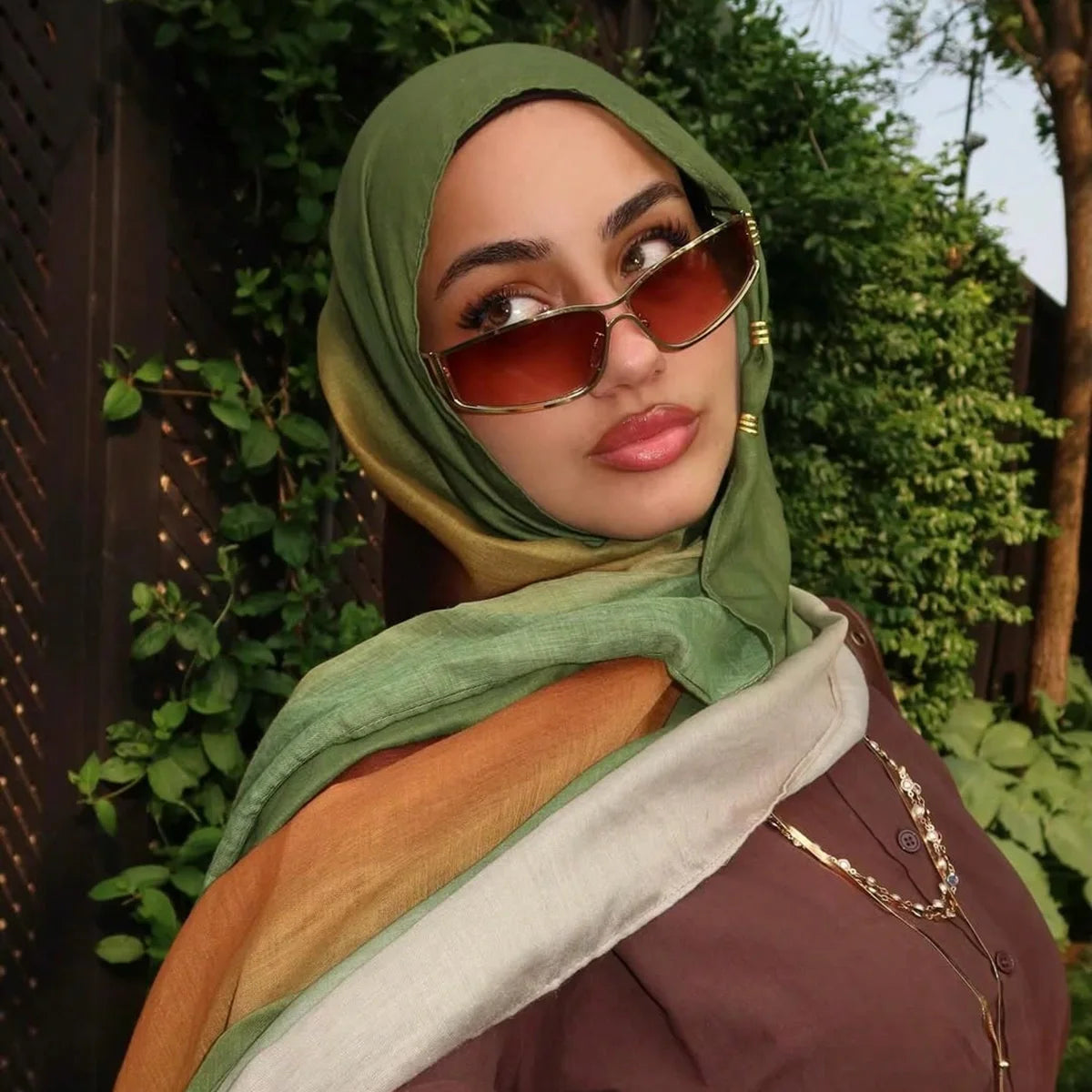 Eine Frau mit grünem Hijab und Sonnenbrille im Freien, umhüllt mit einem orangefarbenen Schal.