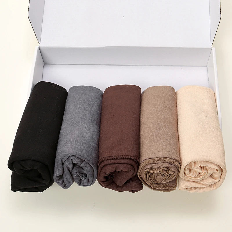Une boîte contenant cinq foulards de hijab de couleur unie roulés en noir, gris, marron, beige et crème.