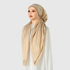 A model wearing an elegant satin silk instant hijab scarf in beige with a gold embellishment.