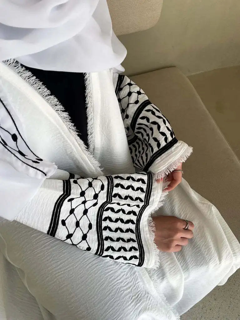 Une femme portant une abaya blanche avec broderie noire et dentelle sur les manches.