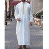 A man wearing a white embroidered thobe or jubah with long sleeves and a vertical gold embellishment.