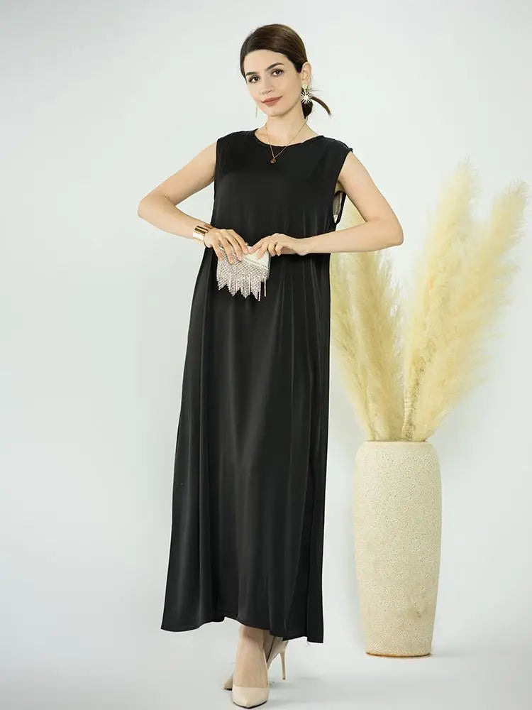 A woman models a black flowing modest abaya dress with silver fringe details against a white background.
