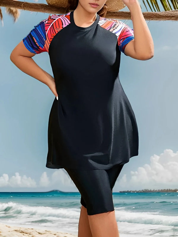 A woman wearing a black print maxi tankini swimsuit set stands outdoors near the ocean.
