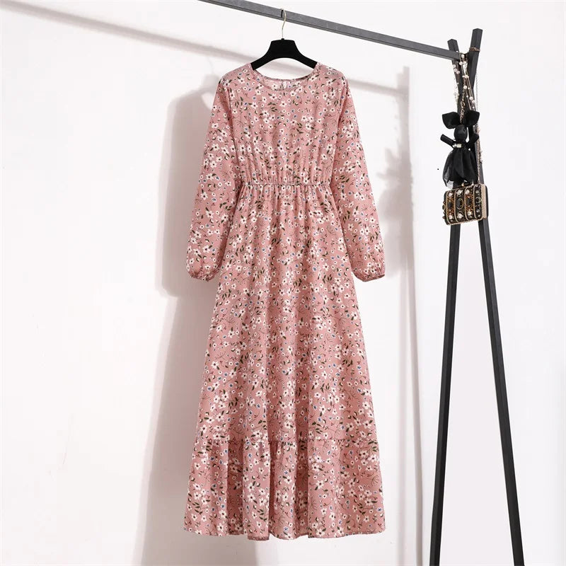 Langes, rosa Blumenmuster-Maxikleid hängt an einem schwarzen Haken vor einer weißen Wand.