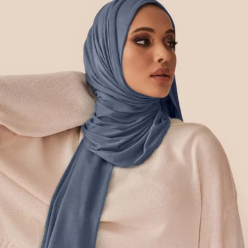 A woman wearing a solid blue soft modal jersey hijab scarf with a light beige top.