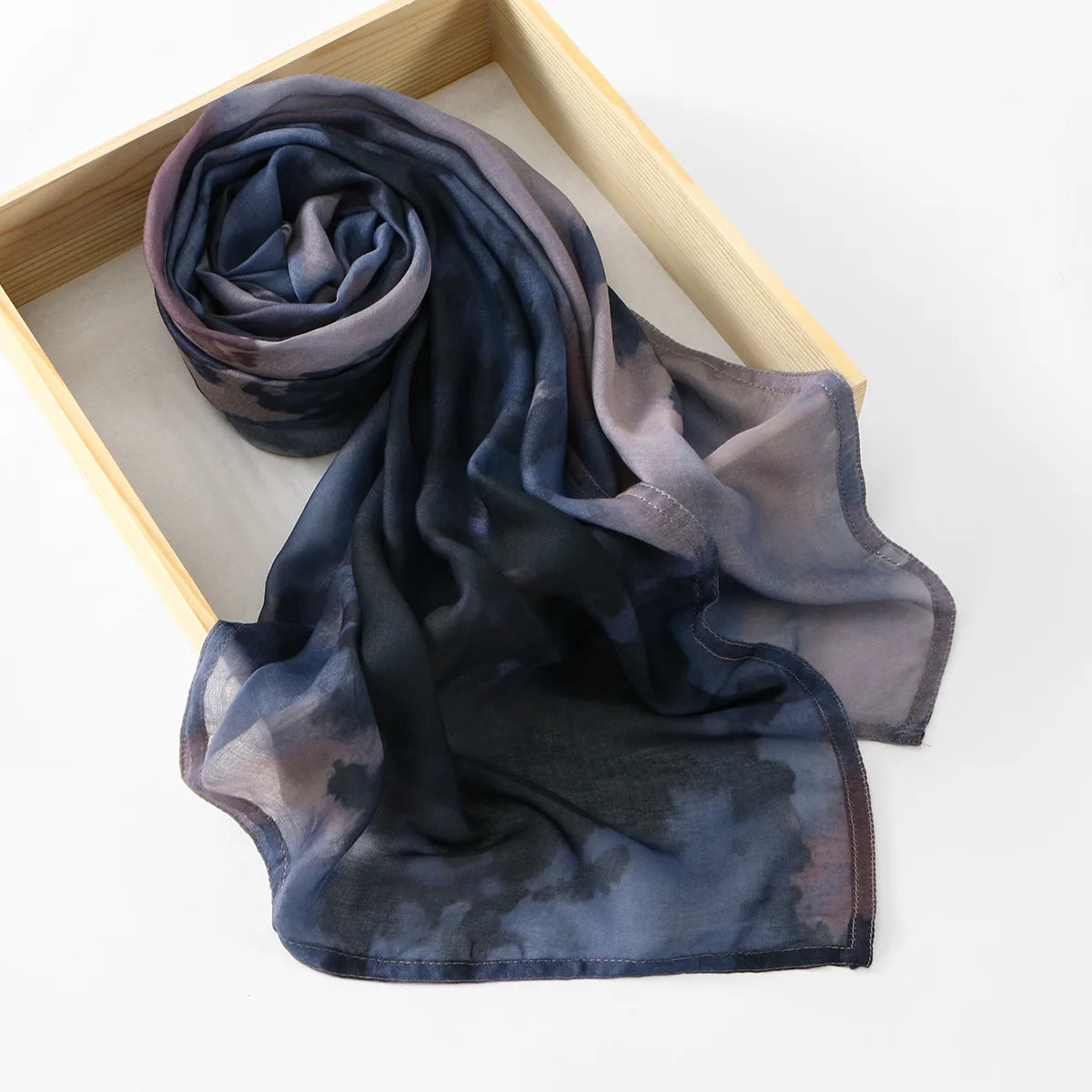 Écharpe de coton à motif floral bleu foncé et gris drapée dans une boîte en bois.