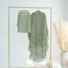 A light sage green ruffled two-layer chiffon hijab displayed on a gold hanger within a rectangular frame.